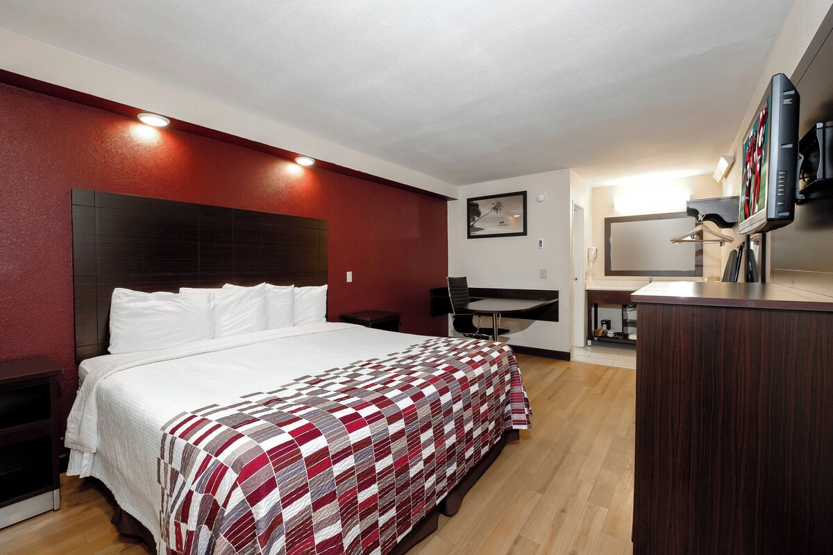 A hotel room with a bed, a desk, a mirror, and a TV.