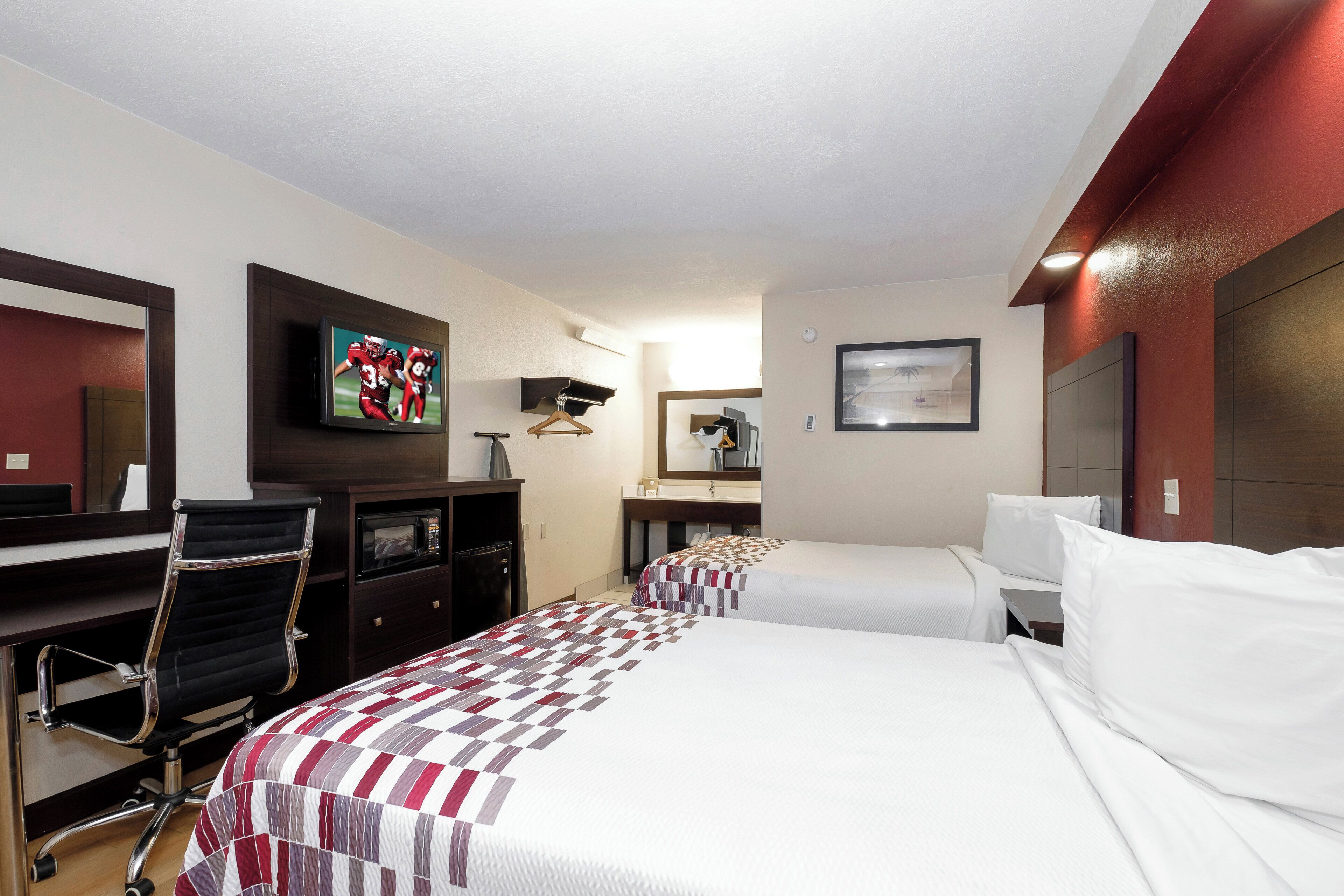 Hotellihuone, jossa on kaksi sänkyä, työpöytä, televisio ja peili.