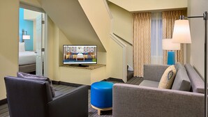 A hotel room with a sofa, ottoman, and a television displaying a room layout. - Sonesta Simply Suites Memphis East Poplar Pike ​ (Memphis)