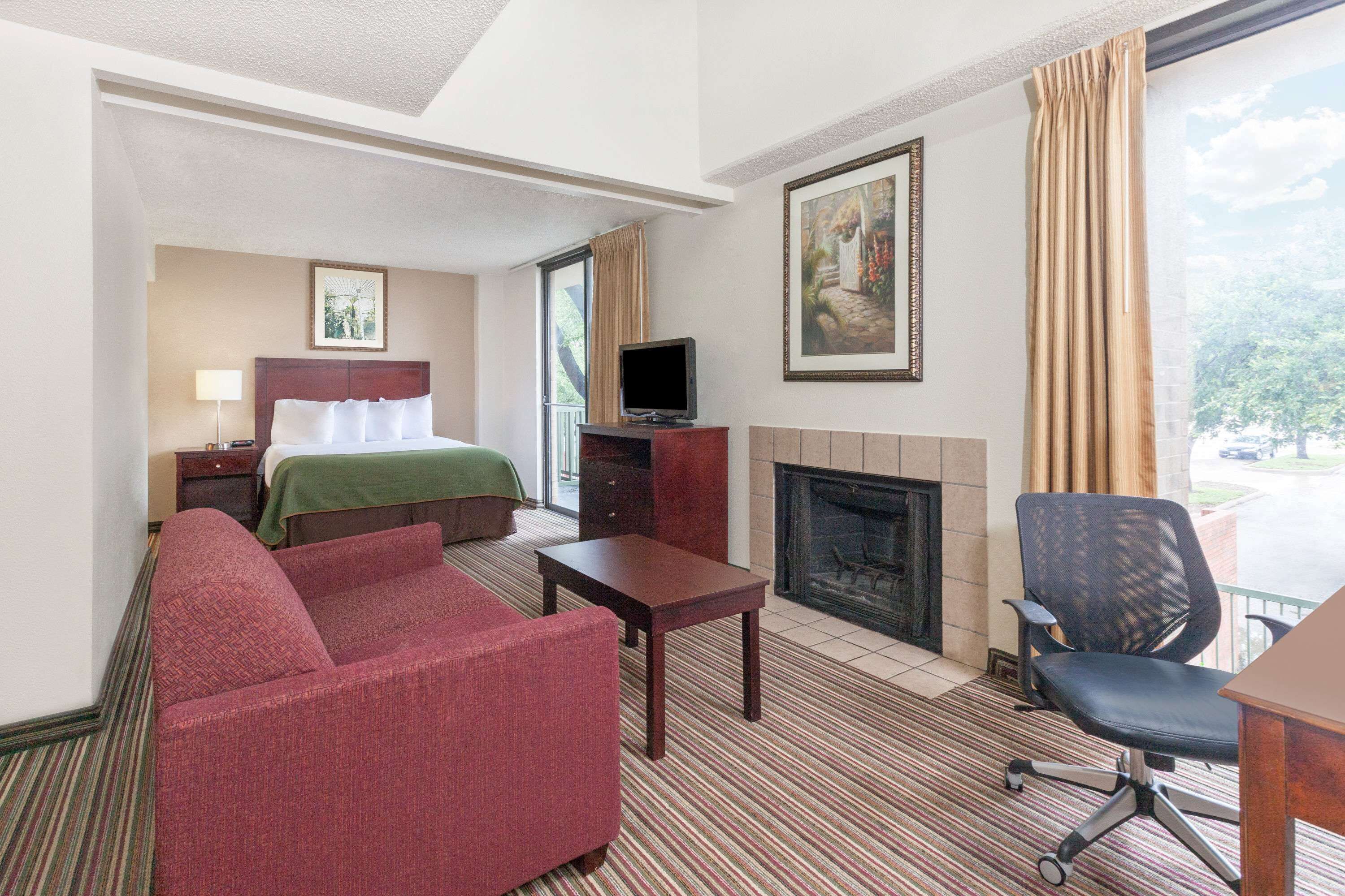 Habitación de hotel con cama, sofá, televisión, chimenea y balcón con cortinas.