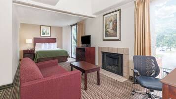 Habitación de hotel con cama, sofá, televisión, chimenea y balcón con cortinas.