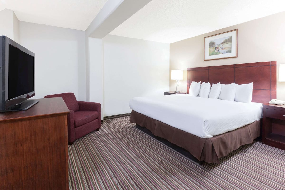 A hotel room with a large bed, a TV on a wooden desk, a red armchair, and a painting on the wall.