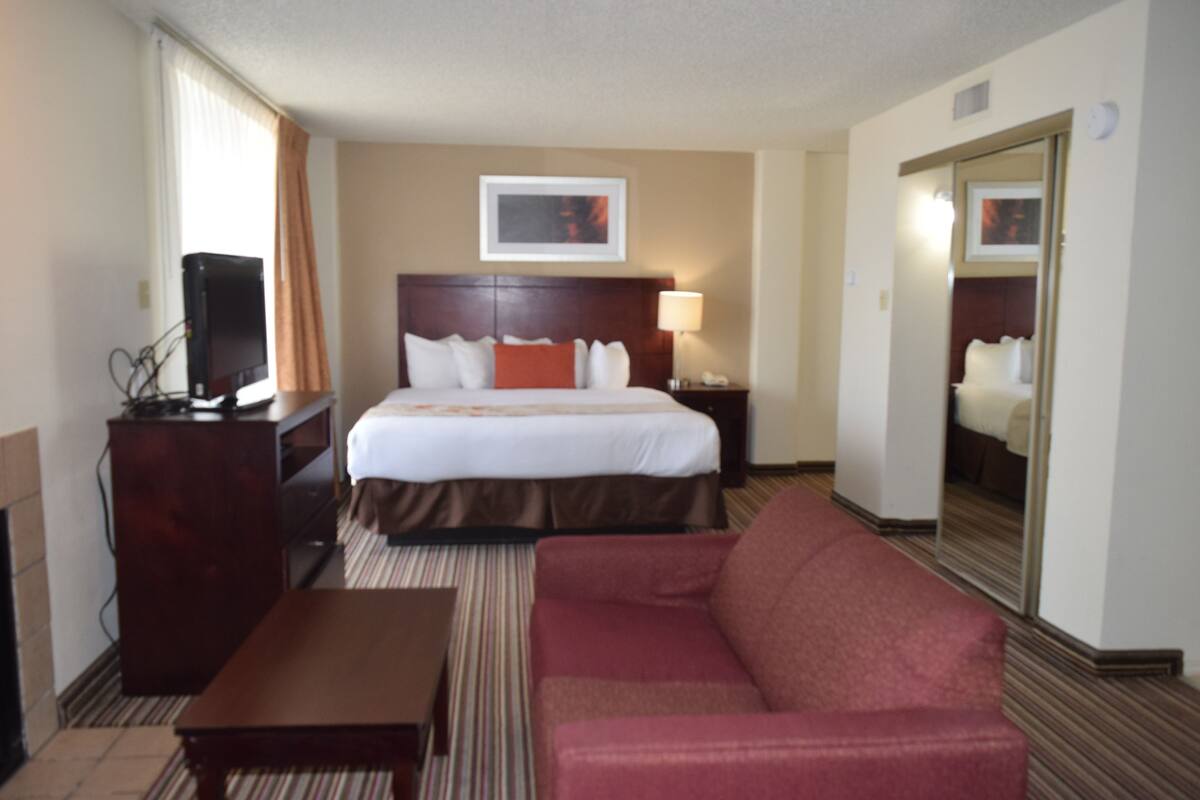 A hotel room with a bed, a desk, a chair, a television, a lamp, and a mirror.