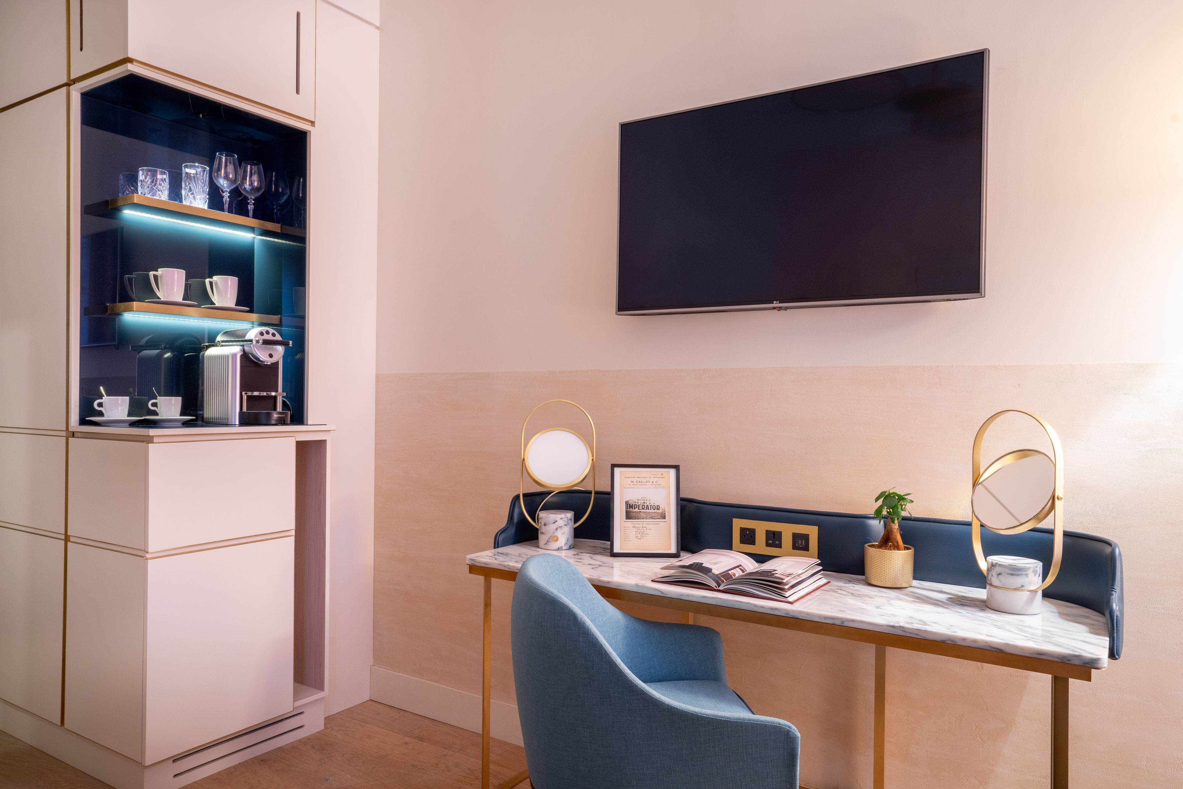 A modern room with a desk, two chairs, a TV, a shelf with glassware, and a plant.