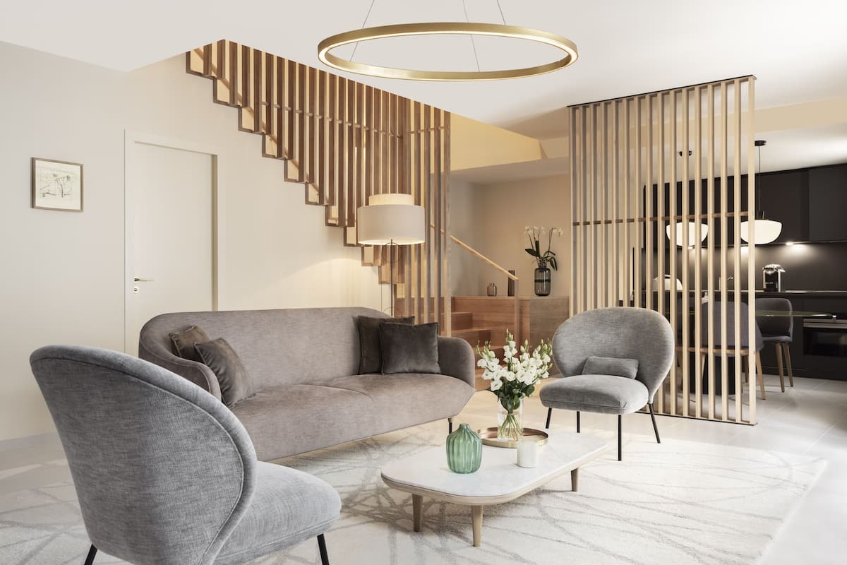 A modern living room with a grey sofa, two armchairs, a coffee table, and a staircase with a wooden railing.