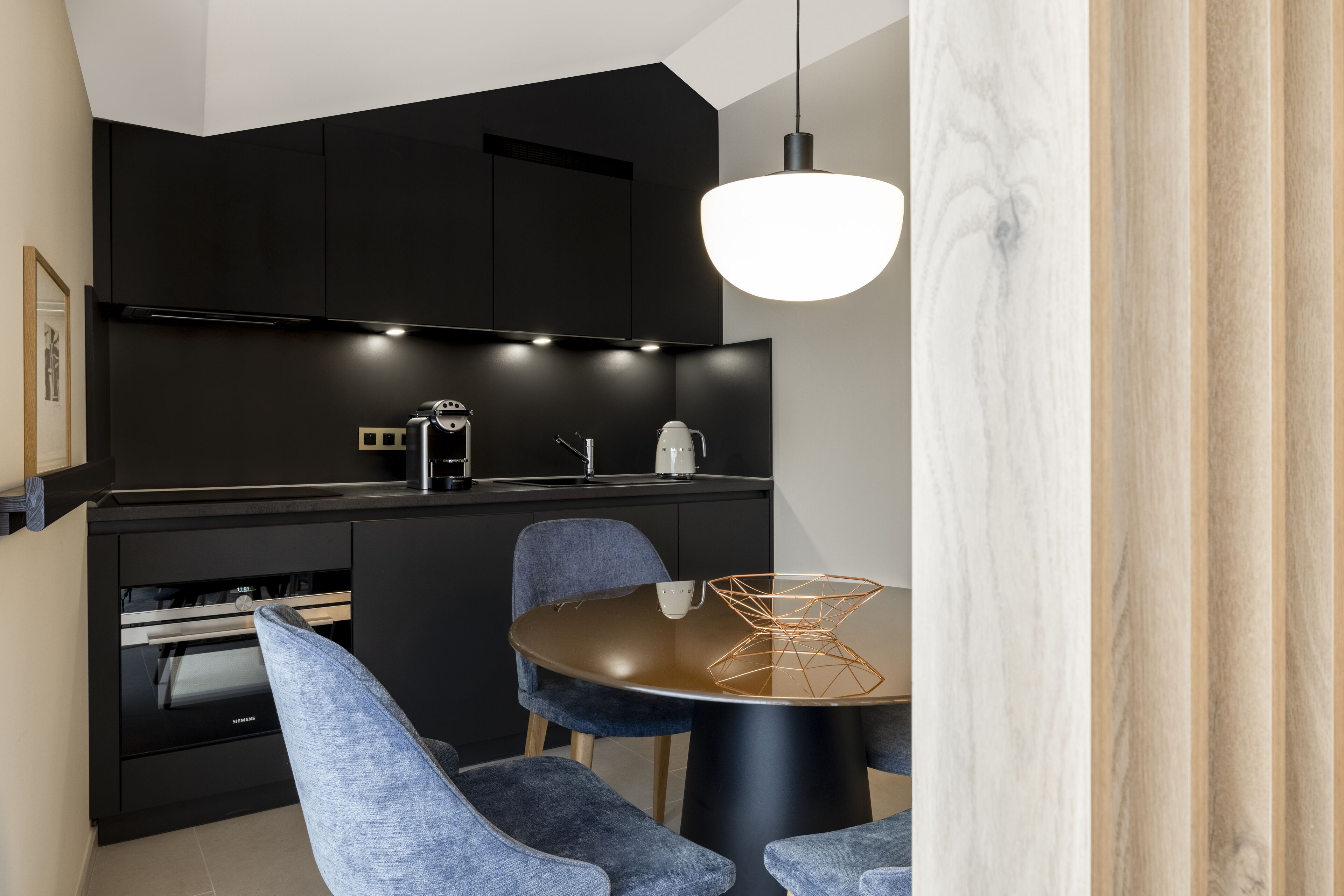 A modern kitchen with dark cabinetry, a round dining table with blue chairs, and a pendant light.
