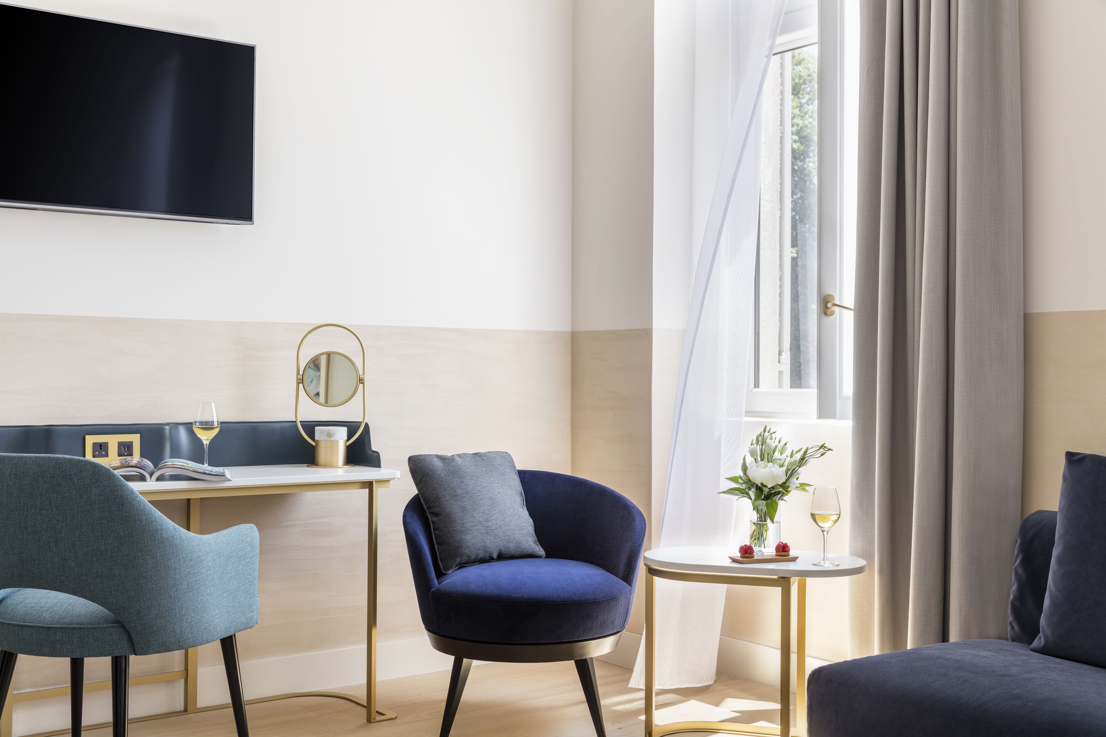 Una habitación de hotel moderna con escritorio, dos sillas, televisor y ventana con cortinas.