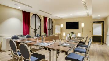 A conference room with a long table, chairs, a whiteboard, a TV, and a projector screen.