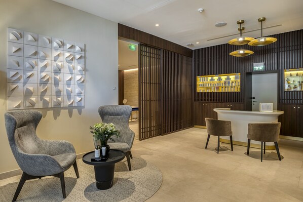 A modern reception area with a reception desk, two armchairs, a coffee table, and a decorative wall panel. - Maison Albar Hotels L'Imperator (Nîmes)