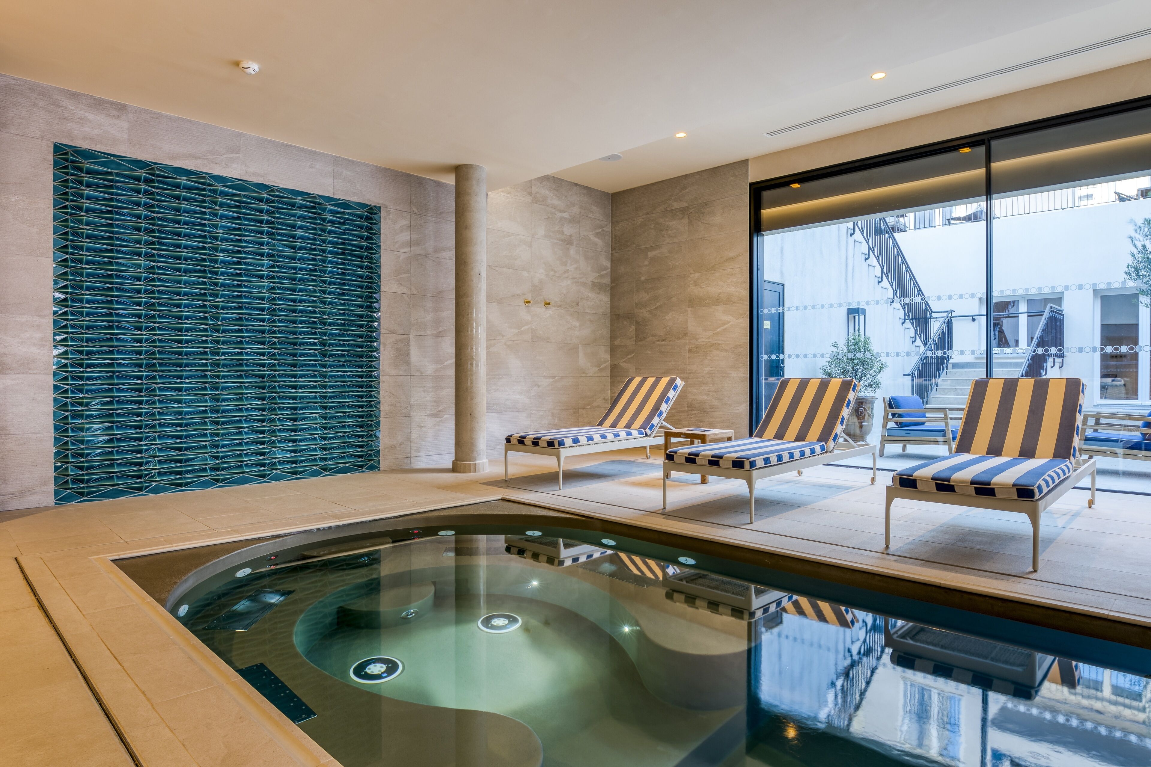 A modern indoor pool area with lounge chairs and a glass-enclosed section.