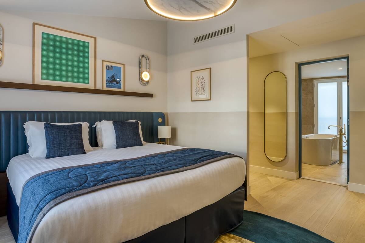 A hotel room with a large bed, a bedside table, a mirror, and a view of the bathroom.