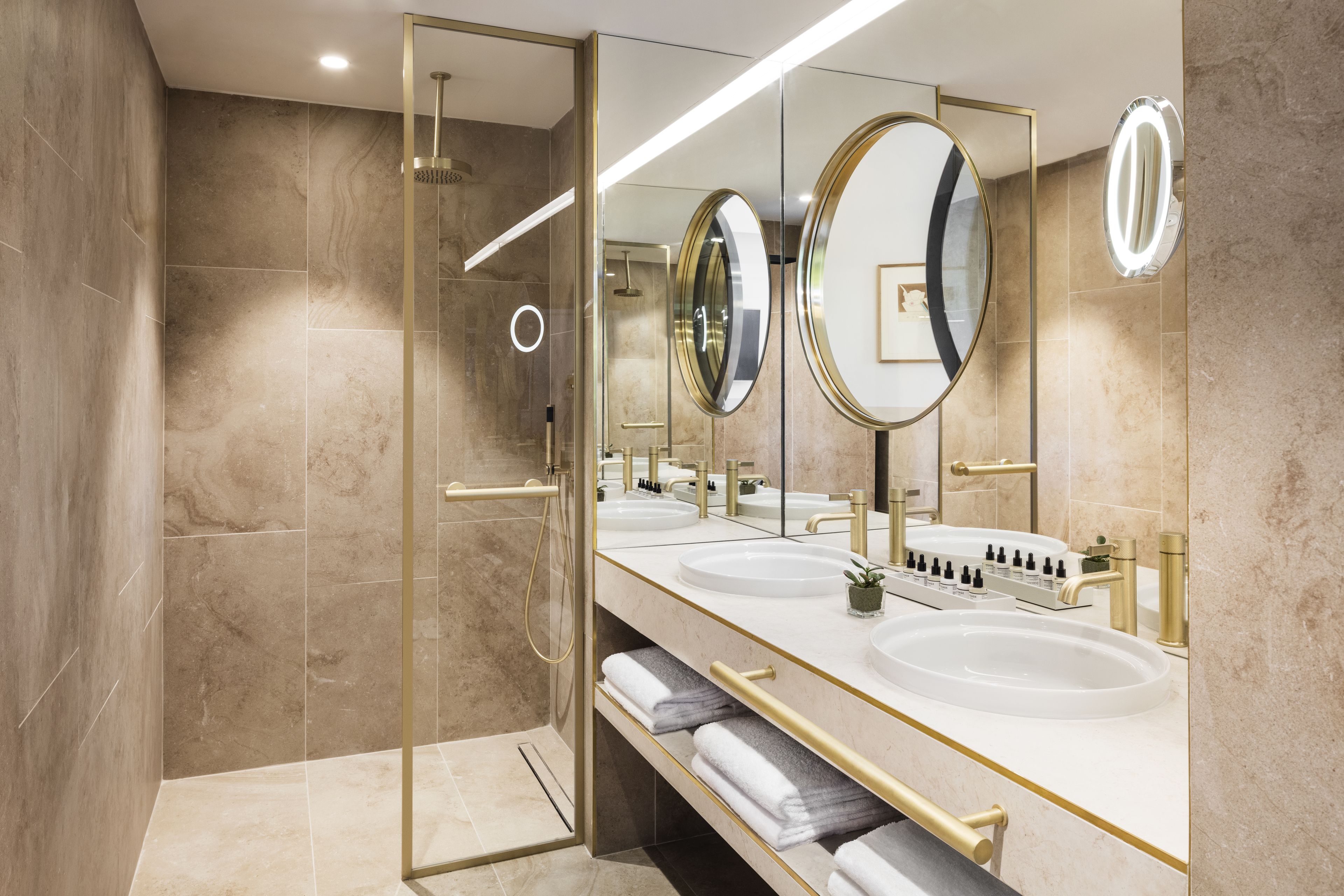 A modern bathroom with three sinks, a glass shower enclosure, and a large mirror with a gold frame.