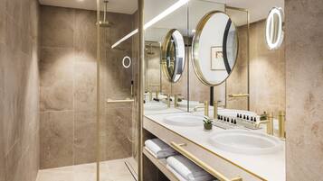 A modern bathroom with three sinks, a glass shower enclosure, and a large mirror with a gold frame.