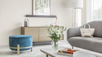 Una sala moderna con un sofá, un reposapiés azul, un jarrón de flores, una lámpara y una estantería.