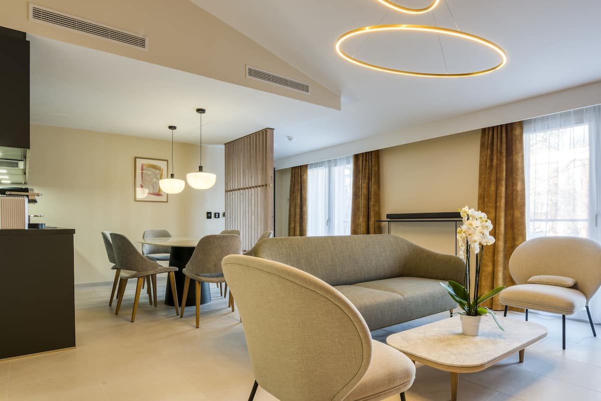 A modern living room with a sofa, armchairs, a coffee table, and a dining area with chairs and a table.