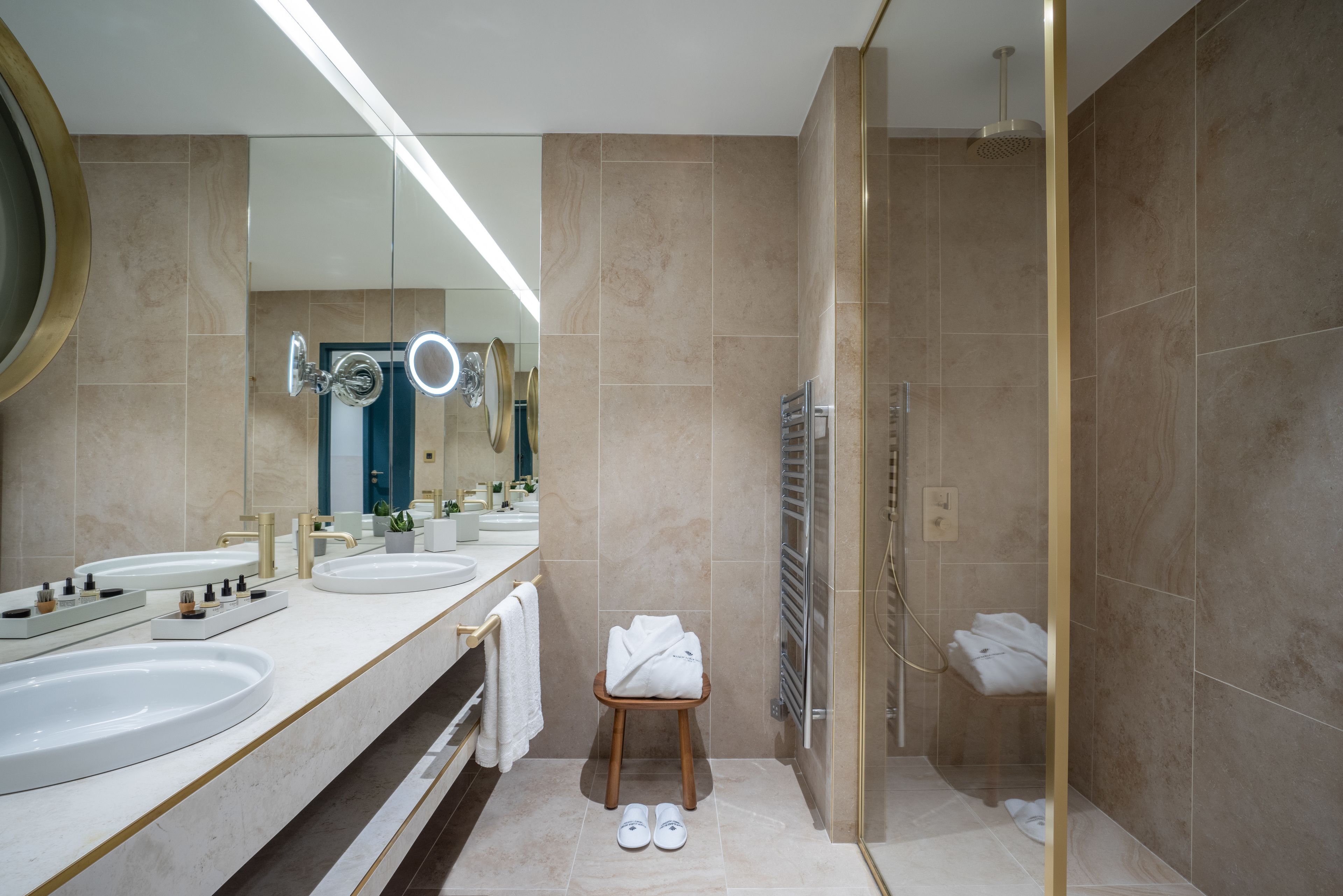 A modern bathroom with two sinks, a mirror, a shower, and a towel rack.