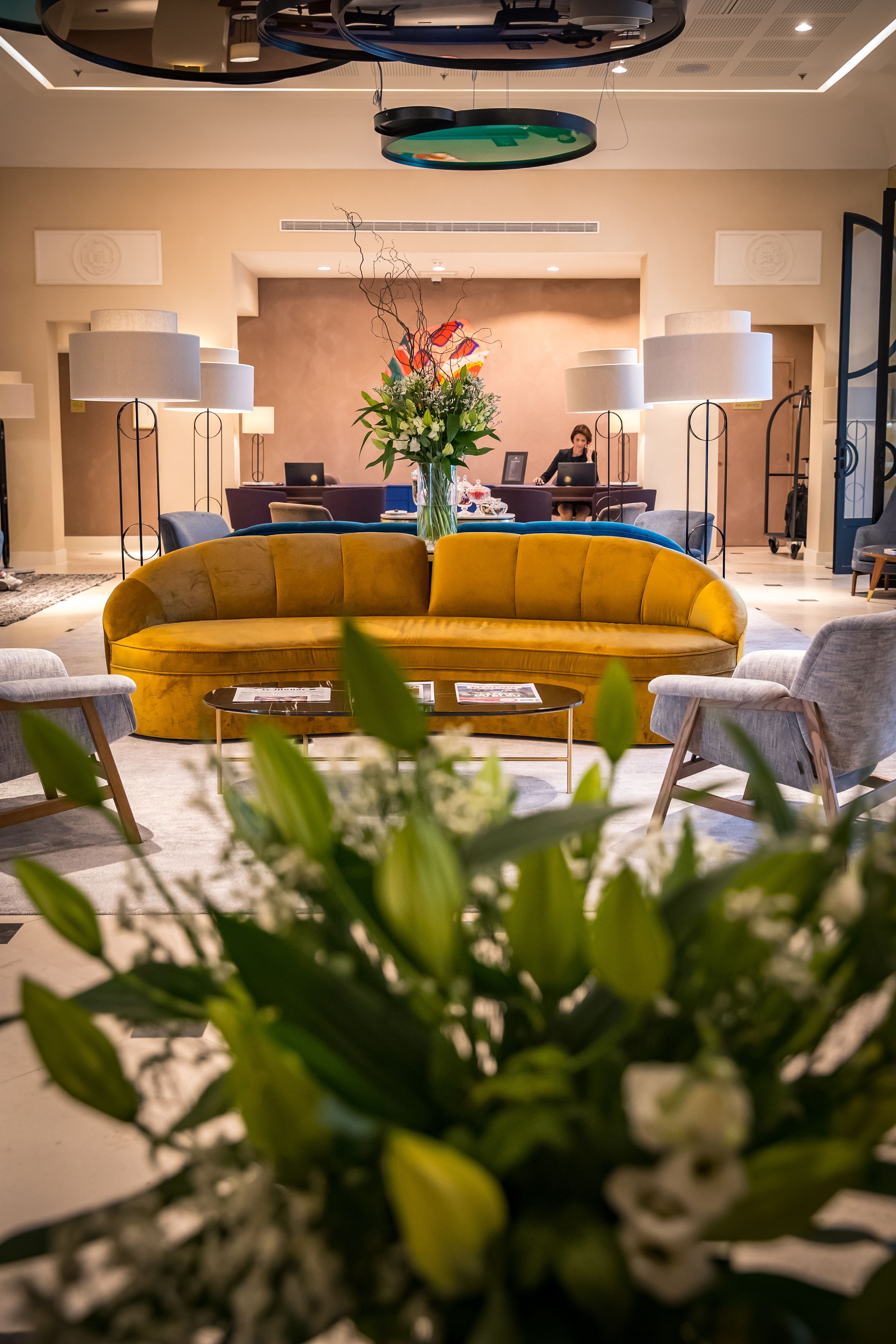 A modern lobby with a yellow sofa, a coffee table, and a large floral arrangement.