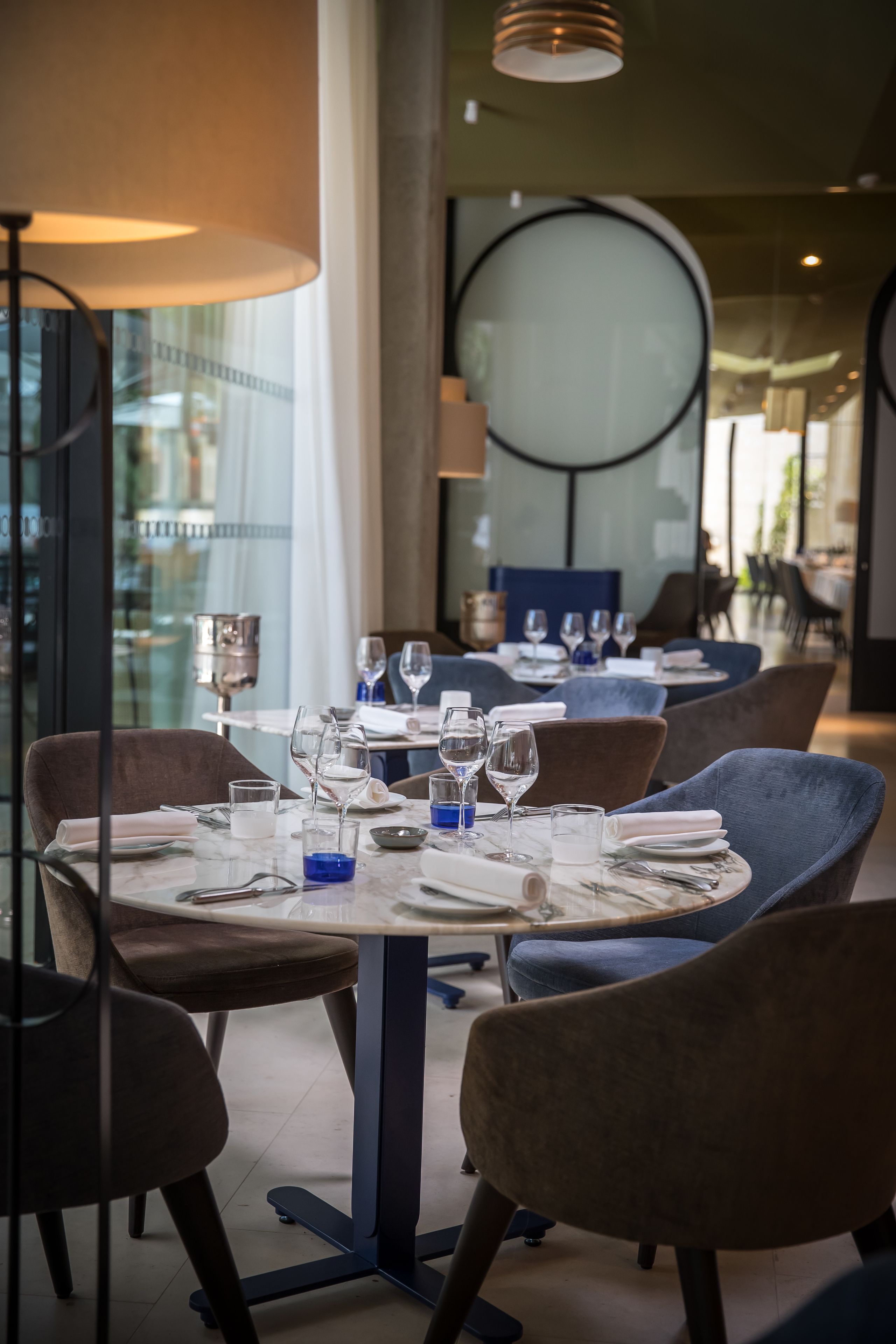 Un interior de restaurante con mesas redondas, sillas y una lámpara de araña moderna.