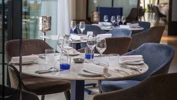 Un interior de restaurante con mesas redondas, sillas y una lámpara de araña moderna.