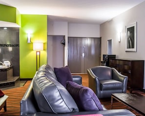 A hotel room with a sofa, armchair, and a small table. There is a lamp, a television, and a door in the background. - Quality Suites Fort Myers I-75 (Fort Myers)