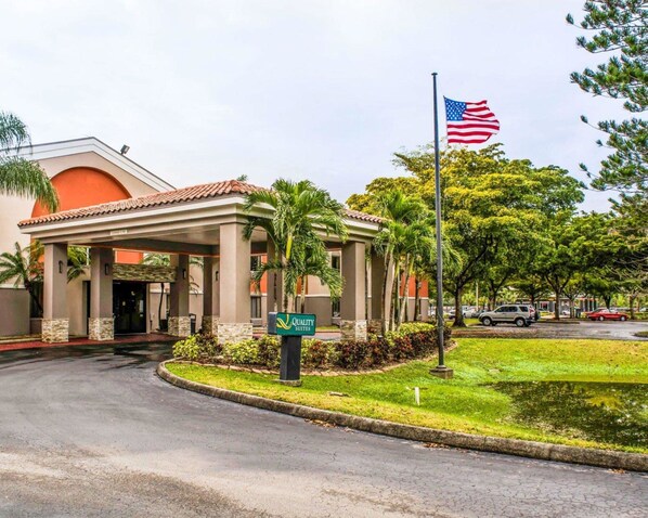 Entrada de hotel con un porche techado, palmeras y la bandera estadounidense.