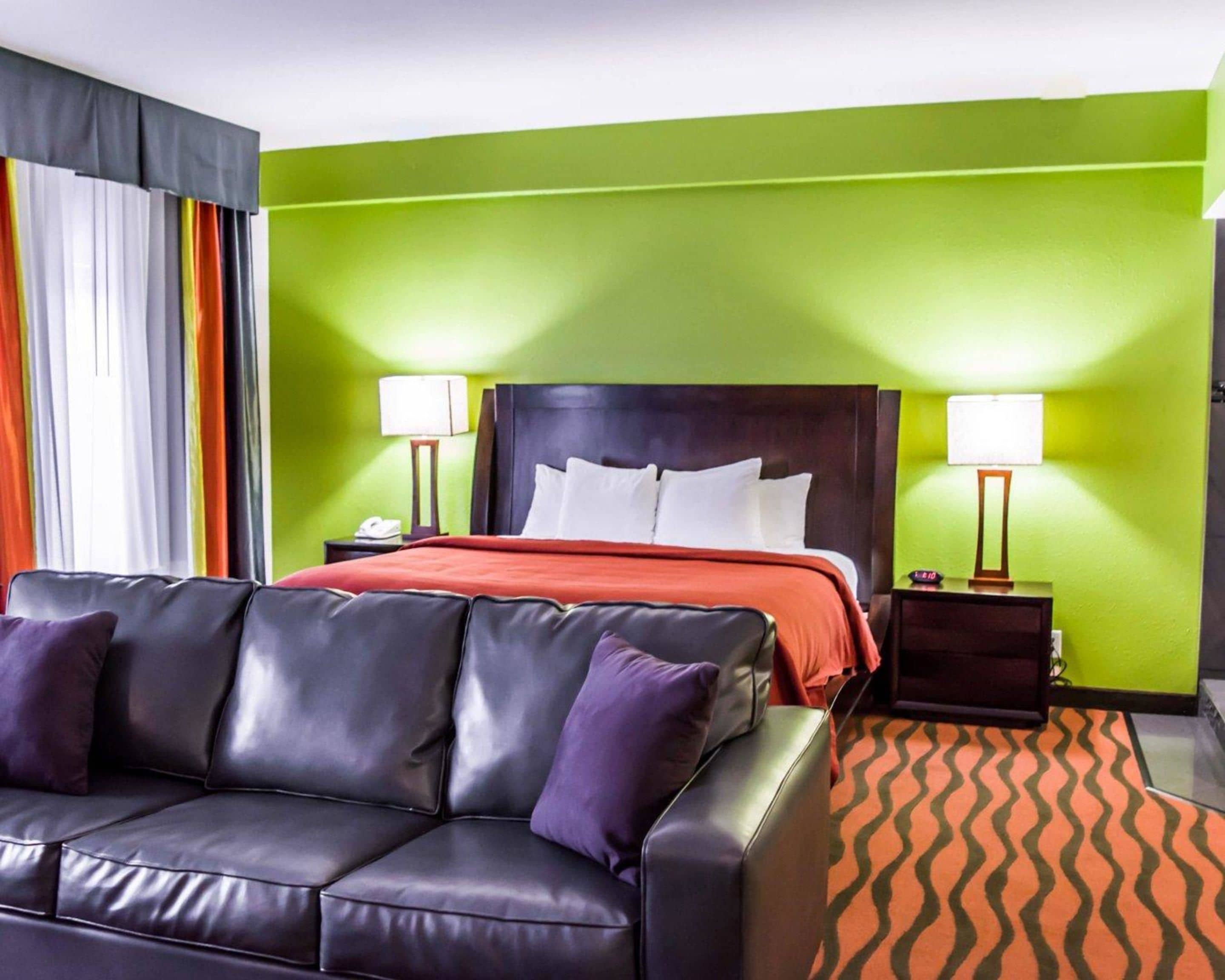 A hotel room with a bed, two bedside tables with lamps, a black leather sofa, and a patterned rug.