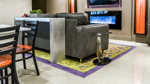 A modern living room with a gray sofa, a TV mounted on the wall, and a fireplace. - Quality Suites Fort Myers I-75 (Fort Myers)