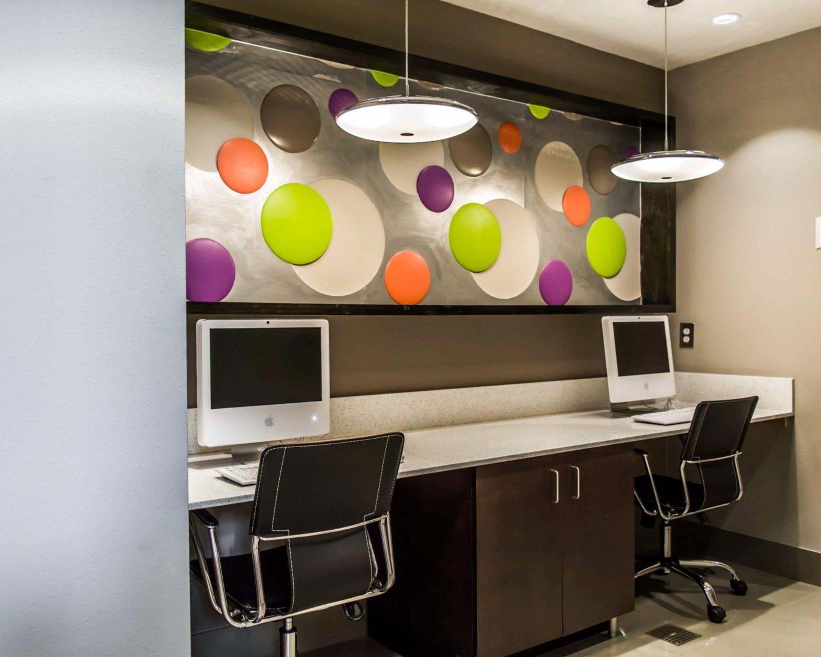 Een modern kantoor met twee bureaus, elk met een computerscherm, zwarte stoelen en een decoratieve wand met ronde patronen.