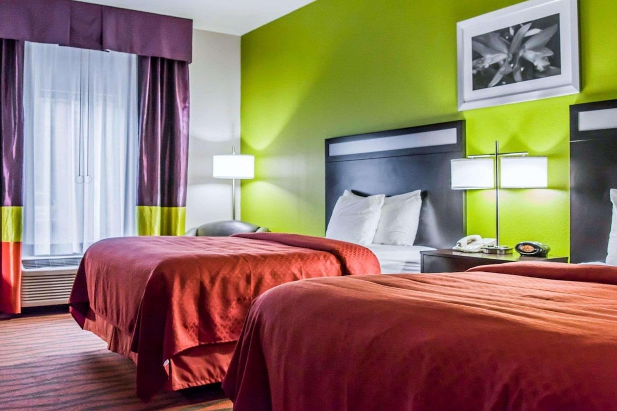 Ein Hotelzimmer mit zwei Betten, einer grünen Akzentwand, einem gerahmten Bild und einem Fenster mit Vorhängen.
