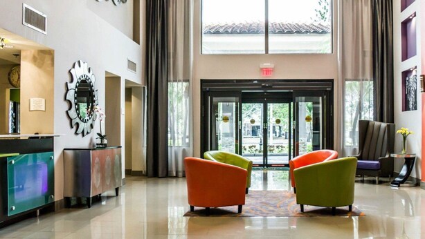 A modern lobby with a reception desk, two colorful armchairs, a large window, and a decorative ceiling light fixture. - Quality Suites Fort Myers I-75 (Fort Myers)