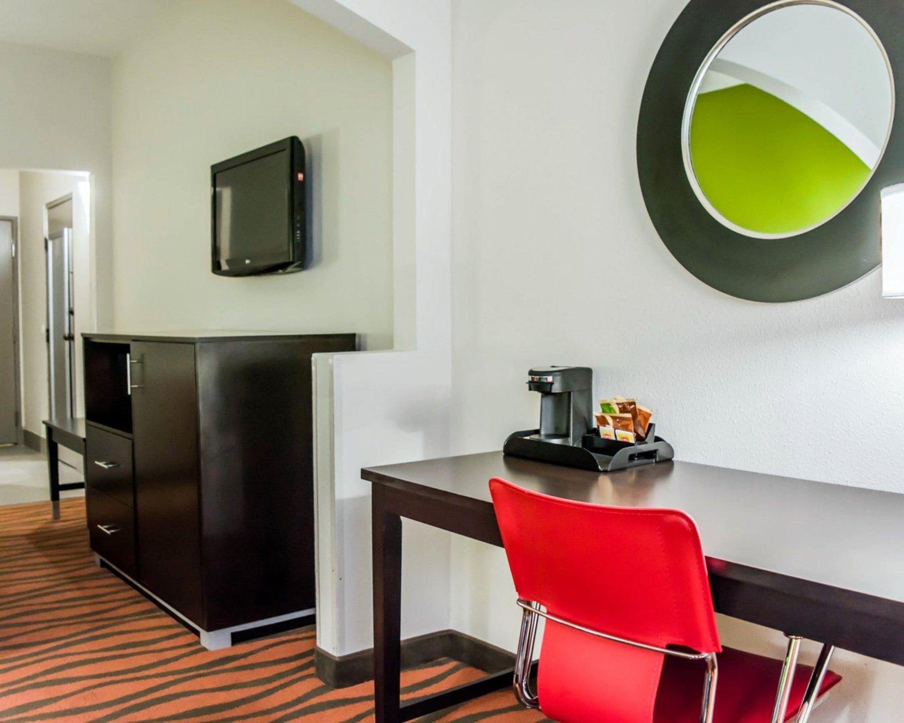 Een hotelkamer met een bureau, een rode stoel, een koffieapparaat, een televisie en een spiegel.