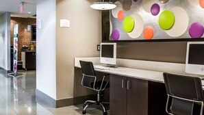 A modern reception desk area with two computer monitors, a black office chair, and a colorful circular wall decoration. - Quality Suites Fort Myers I-75 (Fort Myers)