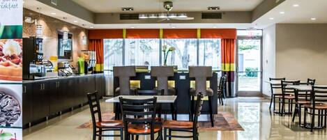 A modern dining area with a central table and chairs, a counter with a coffee machine, and a view of the outdoors.