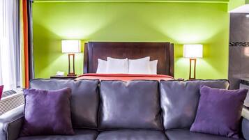 A hotel room with a green wall, a dark wood headboard, a red bedspread, and a black leather sofa with purple cushions.