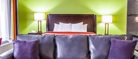 A hotel room with a green wall, a dark wood headboard, a red bedspread, and a black leather sofa with purple cushions.