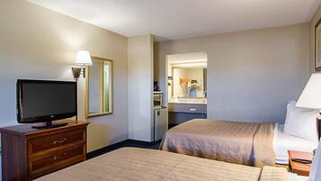 A hotel room with two beds, a TV, a desk, a dresser, and a bathroom visible through an open door.