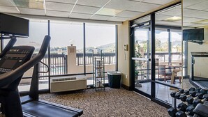 A gym with a treadmill, weights, and a large window offering a city view. - Quality Inn Troutville - Roanoke North (Troutville)