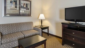 A hotel room with a patterned sofa, a small table, a lamp, a TV on a stand, and a large painting on the wall. - Quality Inn Troutville - Roanoke North (Troutville)
