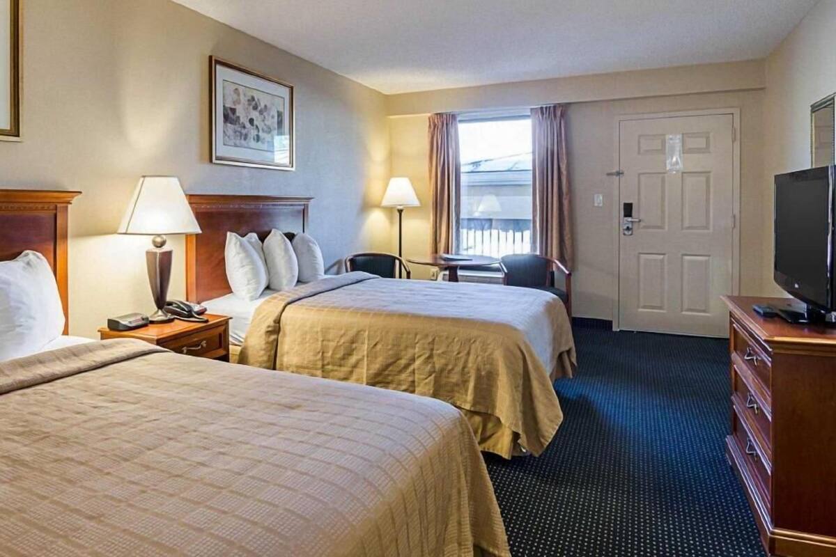 A hotel room with two beds, a desk, a chair, a television, and a door.