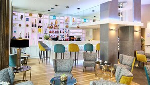 Un moderno vestíbulo de hotel con zona de bar, arreglos de asientos y una pared decorativa con diversos objetos.