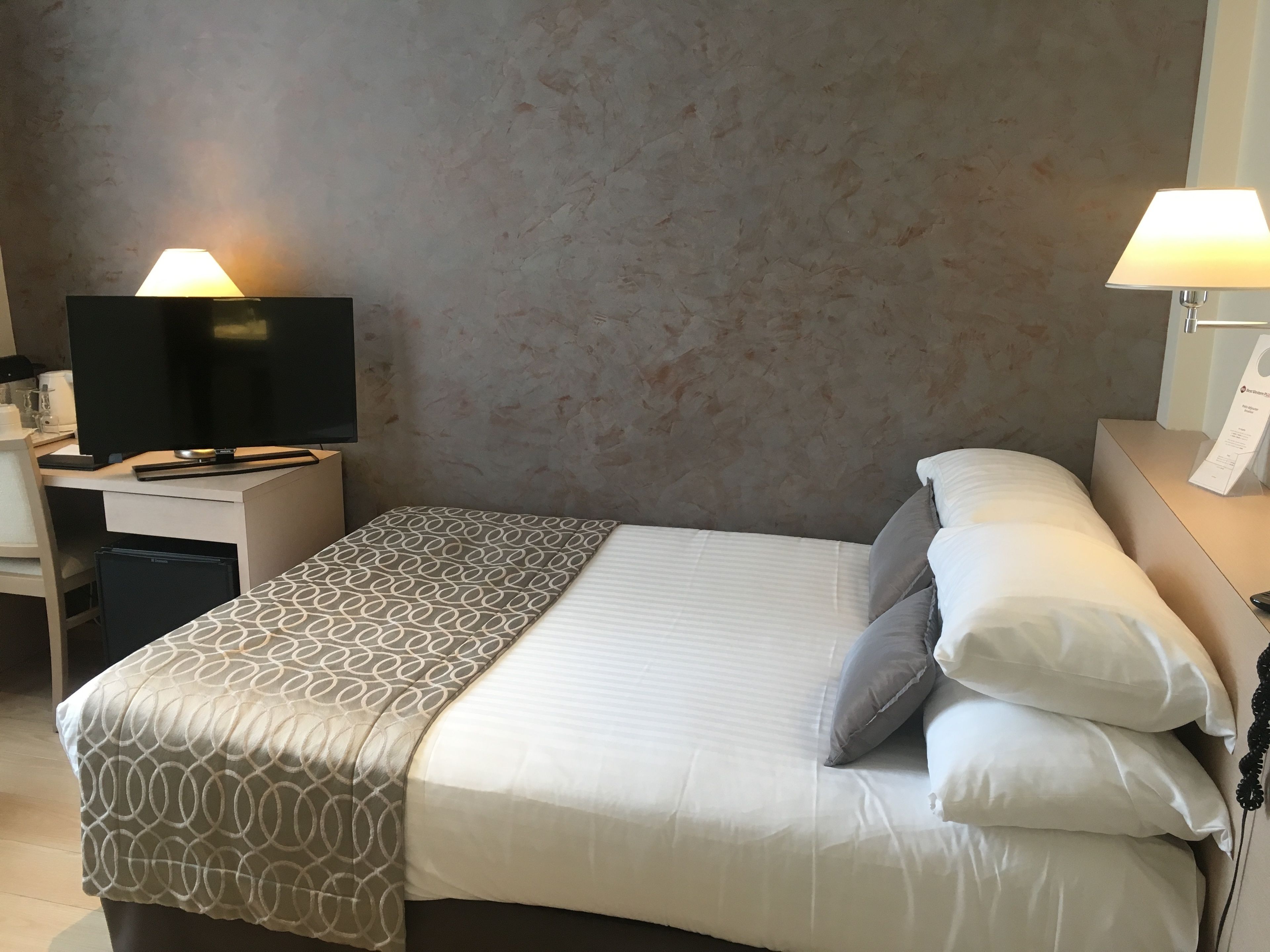 A hotel room with a bed, a desk with a television, and two bedside lamps.
