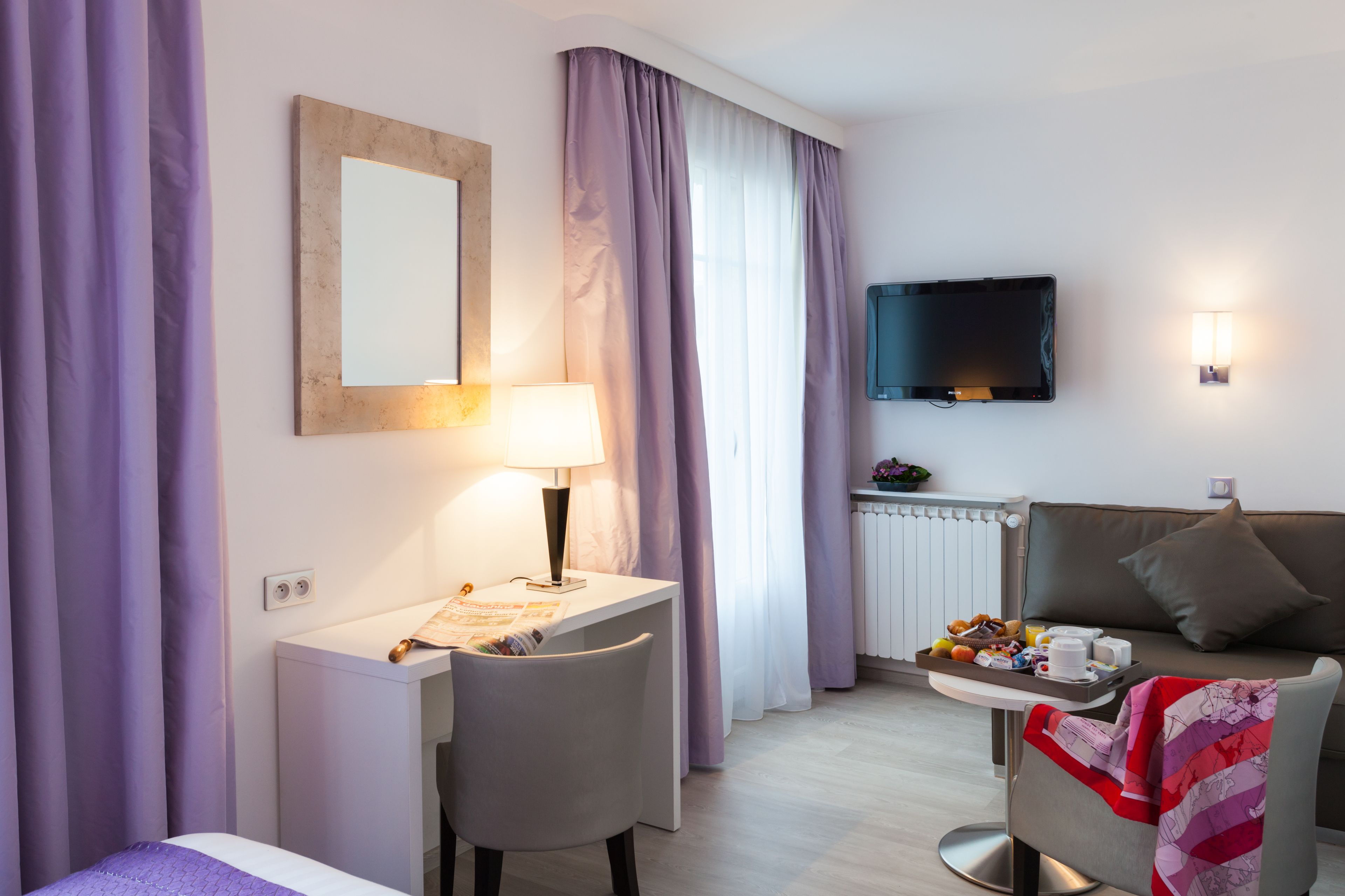 Une chambre d’hôtel comprenant un lit, un bureau avec une lampe, une télévision, un canapé et une petite table avec des articles pour le petit-déjeuner.