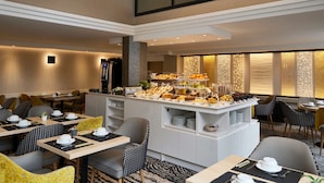 Un comedor de hotel moderno con un bufé central, diversas opciones de asientos y una pared decorativa con textura.