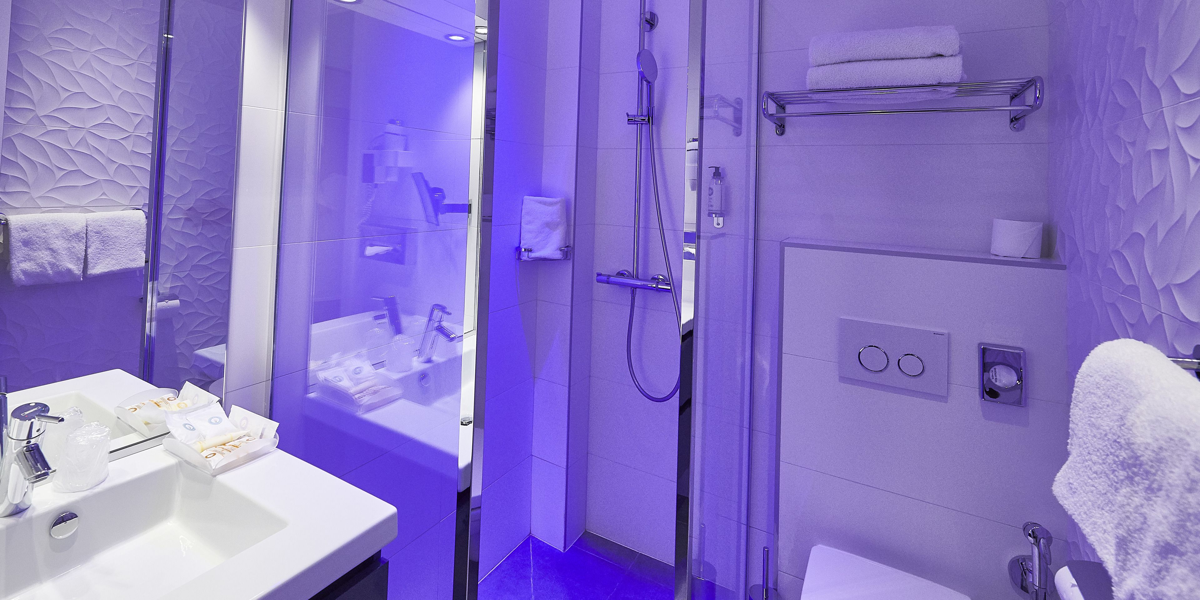 A modern bathroom with a glass-enclosed shower, a white sink with toiletries, and a towel rack.