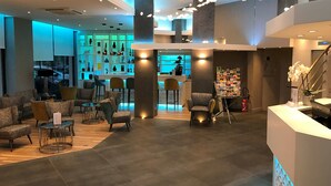 Un moderno vestíbulo de hotel con zonas de estar, una recepción y un bar.