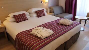 A hotel room with a large bed, two pillows, a bedside table with a lamp, a chair, and a small round table.