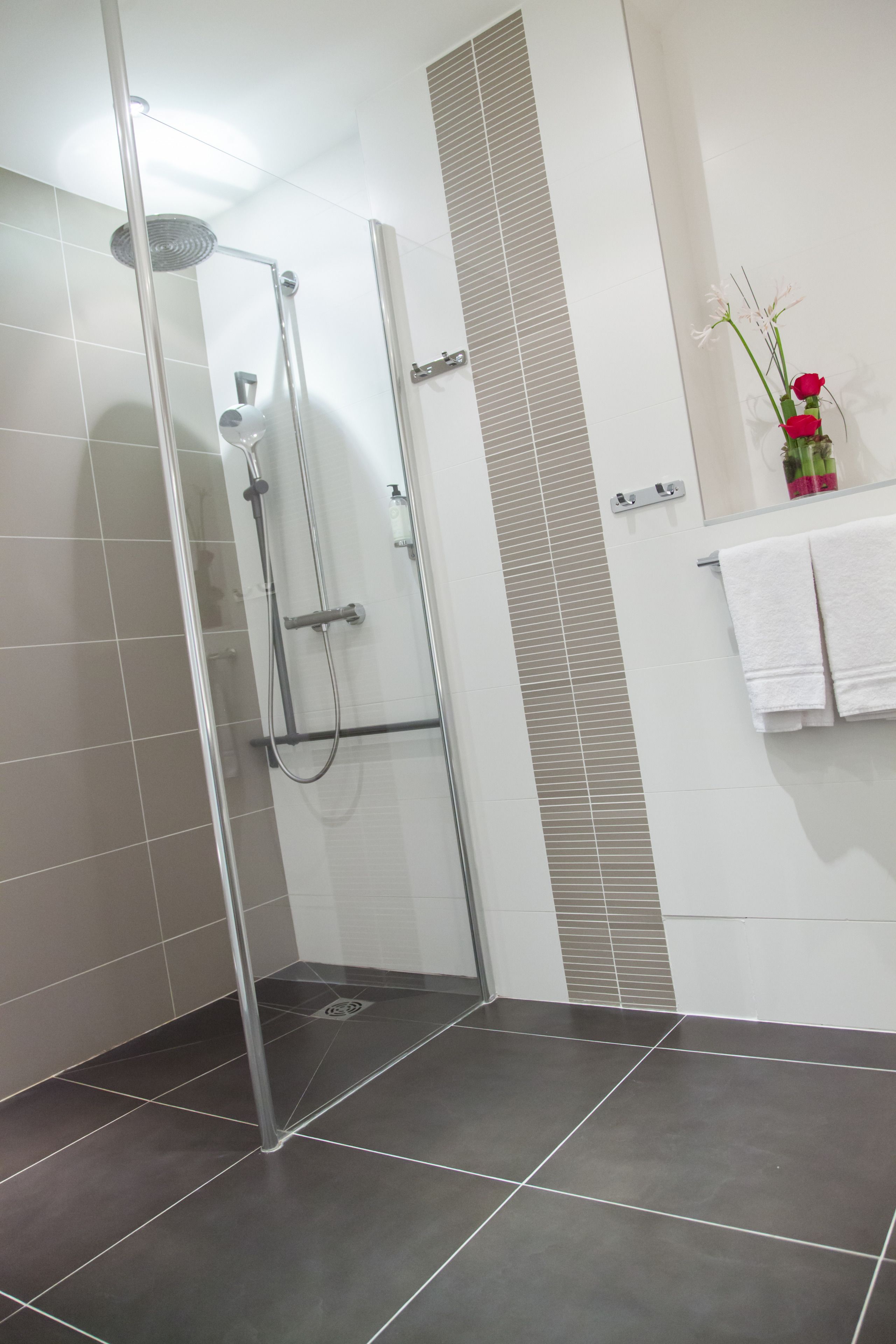 Ein modernes Badezimmer mit einer Glaskabine zur Dusche, gefliesten Wänden und einem weißen Handtuchhalter.