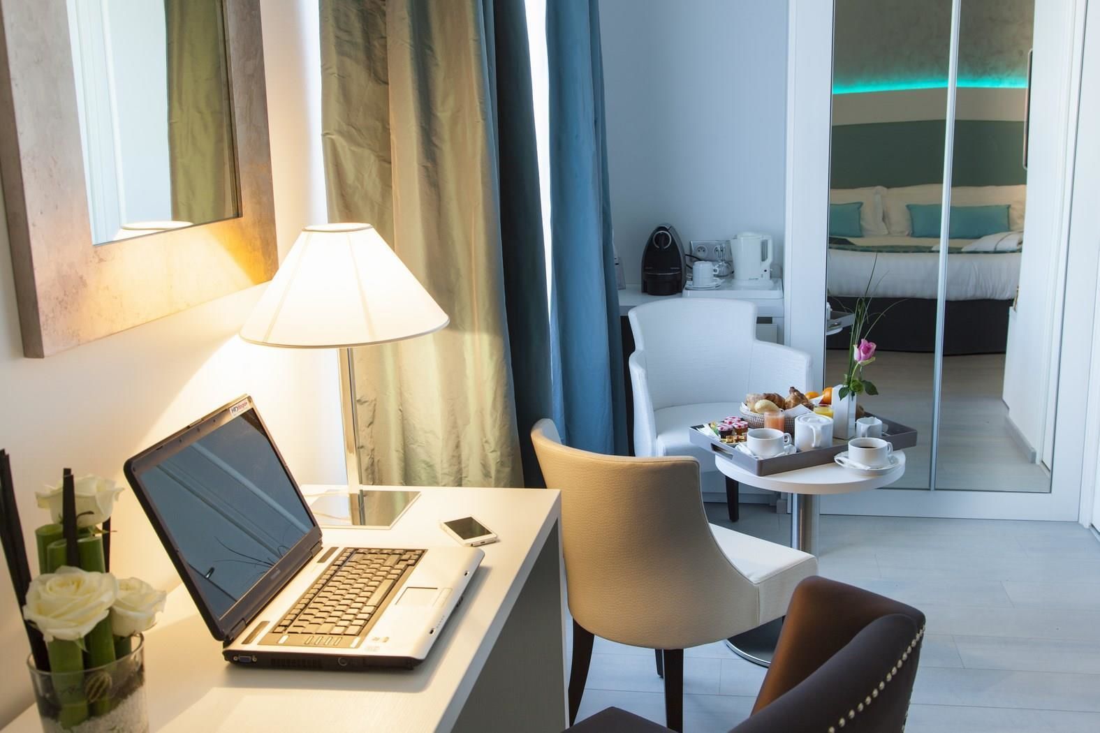 Une chambre d’hôtel équipée d’un bureau, d’un ordinateur portable et d’un coin repas où sont servis les articles du petit-déjeuner.