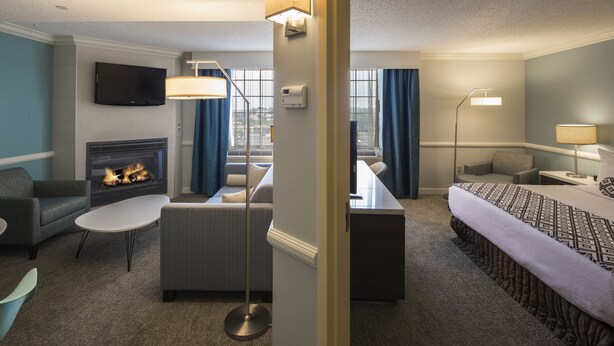A hotel room with a fireplace, a sofa, a bed, a desk, and a TV. - Crowne Plaza Suites Pittsburgh South by IHG (Bethel Park)
