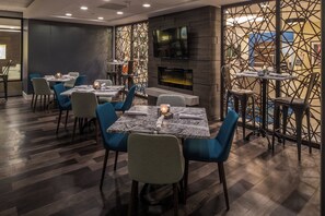 A restaurant interior with tables, chairs, a TV, and a patterned wall. - Crowne Plaza Suites Pittsburgh South by IHG (Bethel Park)
